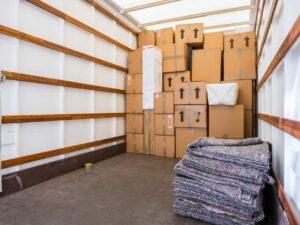 Three people loading boxes and furniture into a moving truck on a sunny day.