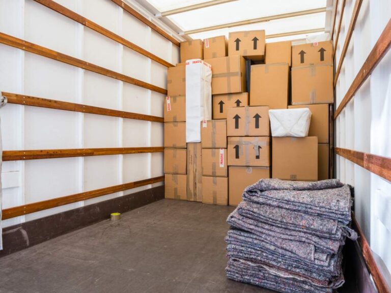Three people loading boxes and furniture into a moving truck on a sunny day.